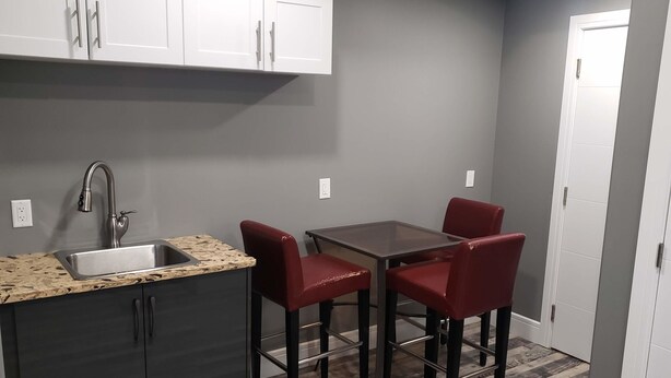 A compact kitchen with a sink, a dining table, and two red chairs.