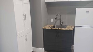 A compact kitchen with white cabinets, a granite countertop, a sink, and a refrigerator.