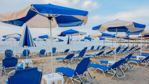 A beach with rows of blue lounge chairs and white sunbeds, some under blue and white umbrellas. - Mikes Beach Lux (Hersonissos)