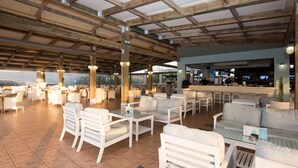 A spacious outdoor seating area with white furniture and a bar in the background. - Mikes Beach Lux (Hersonissos)