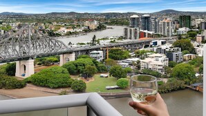Ein Balkon mit einem Weinglas, mit Blick auf eine Skyline inklusive Brücke, Gebäude und Grünflächen.