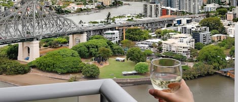 A balcony with a glass of wine, overlooking a cityscape with a bridge, buildings, and greenery.