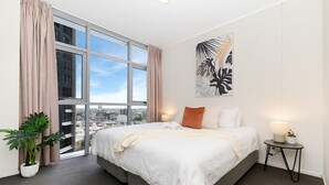 Ein modernes Hotelzimmer mit einem großen Bett, Blick auf die Stadt, einer Zimmerpflanze und einem Wandbild.