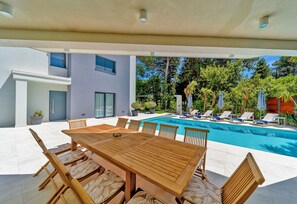 A modern outdoor pool area with a wooden table and chairs, lounge chairs, and a clear view of the pool.