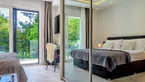 A modern bedroom with a large bed, a desk, and a balcony with a view of greenery.