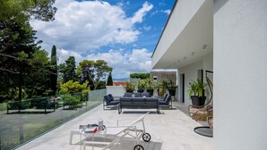 A modern outdoor patio with a glass balustrade, a seating area with sofas and chairs, and potted plants.