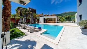 A modern pool area with lounge chairs, a barbecue area, and a view of a mountain.