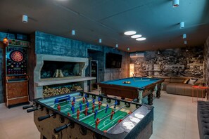 A room with a foosball table, dartboard, and billiards table.