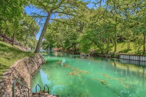 A river with clear water, surrounded by trees and a stone wall. - Fun on the Comal CW C104 2 Bedroom Condo by RedAwning (New Braunfels)