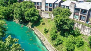 Un immeuble moderne à plusieurs étages, doté de balcons, situé à proximité d’une rivière aux eaux turquoise.