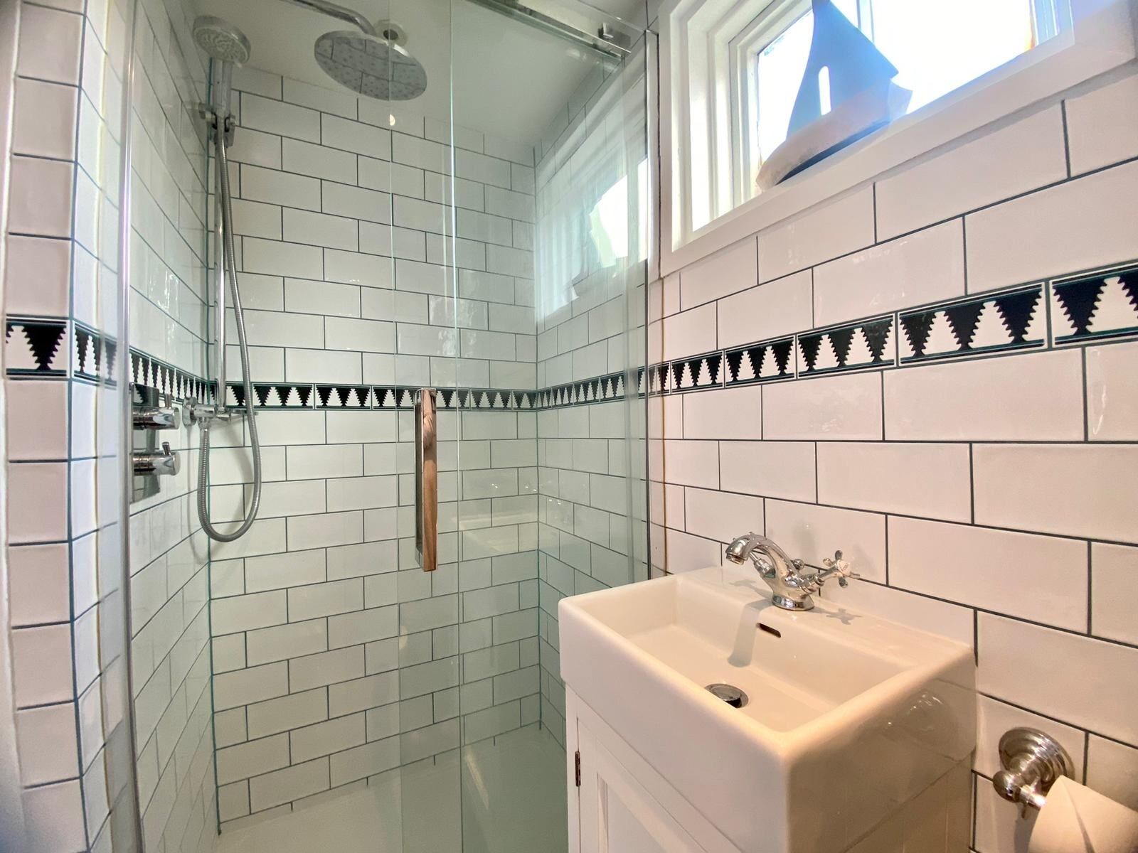 Ein Badezimmer mit weißen Fliesen, einer Glasdusche und einem Waschbecken mit Spiegel.