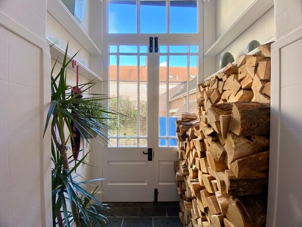 A hallway with a white door, a large window, and a stack of firewood.