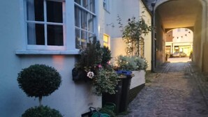 A narrow cobblestone alleyway with a building on the left featuring a window and potted plants. - Beautiful 17th Century Coach House (Marlborough)
