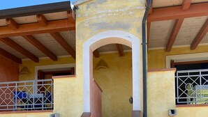 Eine geschwungene Treppe führt zu einem Balkon im zweiten Stock mit Metallgeländer, einer Holztür und einem kleinen Blumentopf.