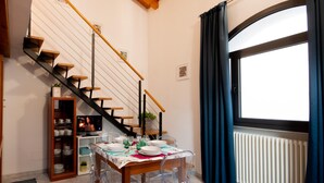 A dining area with a table set for four, a wooden staircase, and a window with curtains.