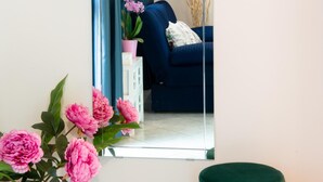 A mirror reflecting a blue sofa, a pink flower arrangement, and a green ottoman.
