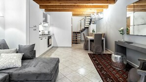 A modern living room with a grey sofa, a dining area with a table and chairs, a kitchen with white cabinets, and a staircase leading to an upper floor. - Starfish 4         . (Venezia)