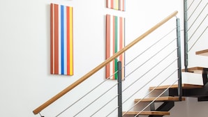 A staircase with wooden steps and metal railings, a red table with a metal bowl, and colorful vertical stripes on the wall.