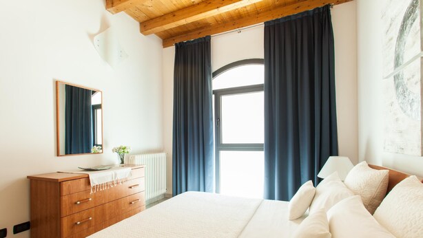 A bedroom with a large bed, a wooden dresser, a mirror, and a window with curtains. - Starfish 2 . (Venezia)