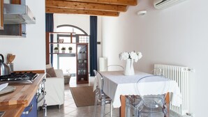 A modern kitchen with wooden beams, a dining area with a white table and chairs, and a view through a glass door to a balcony. - Starfish 2 . (Venezia)