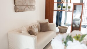 A modern living room with a white sofa, decorative pillows, a wicker basket, and a view of a dining area through a glass door. - Starfish 2 . (Venezia)