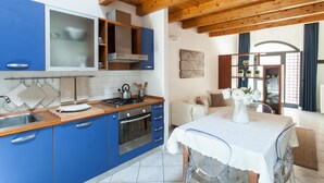 A modern kitchen with blue cabinets, a wooden ceiling, and a dining area with a table set for two. - Starfish 2 . (Venezia)