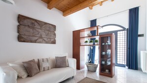 A living room with a white sofa, a wooden cabinet with glass doors, a world map artwork, and a window with blue curtains. - Starfish 2 . (Venezia)