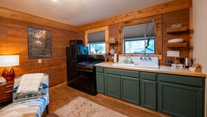 A kitchen with wooden walls, a stove, refrigerator, and a window with blinds.
