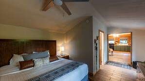 A bedroom with a large bed, a wooden headboard, a bedside table with a lamp, and a ceiling fan.