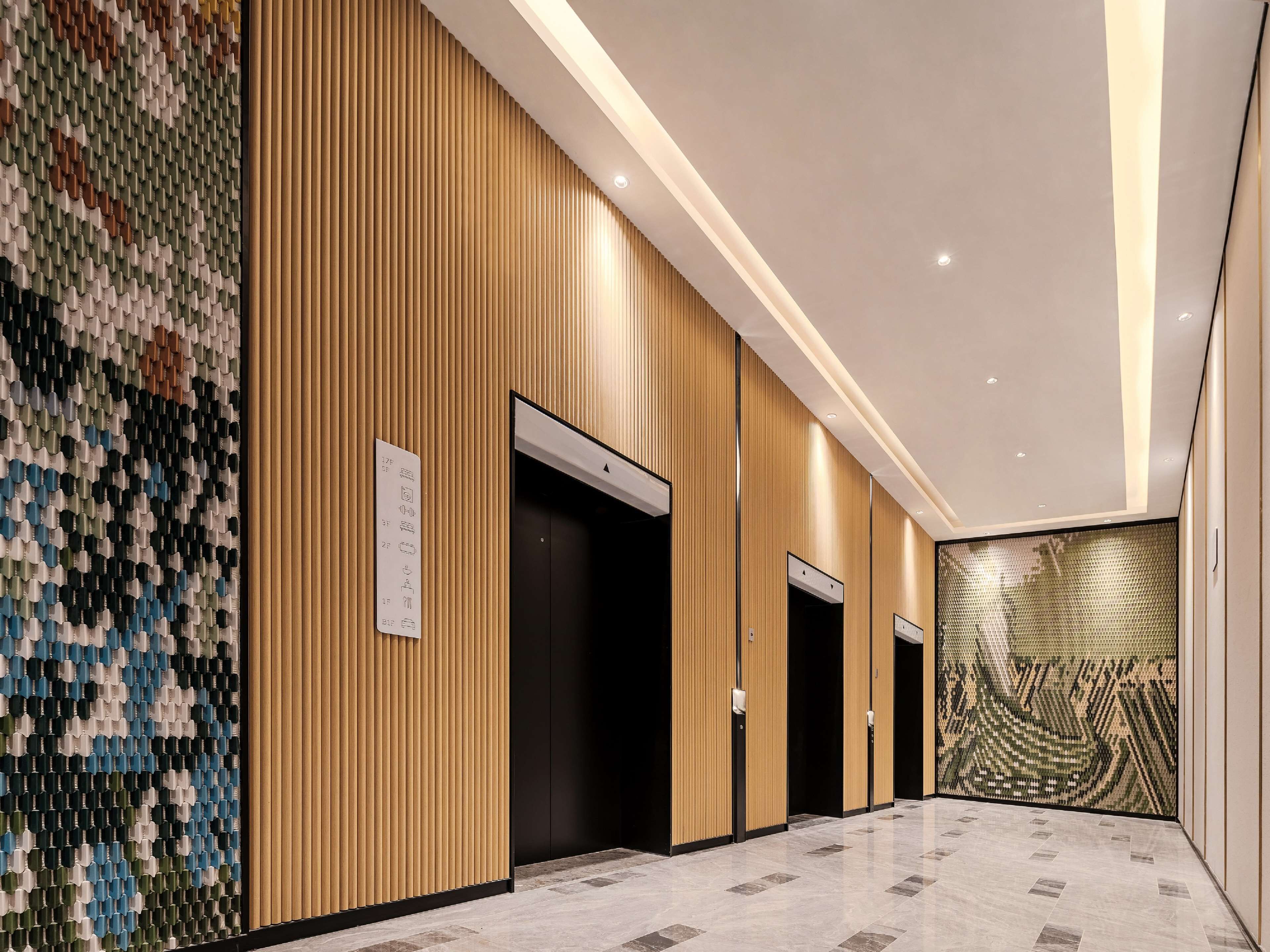 A modern hotel lobby with wooden paneling, three elevators, and a patterned wall.
