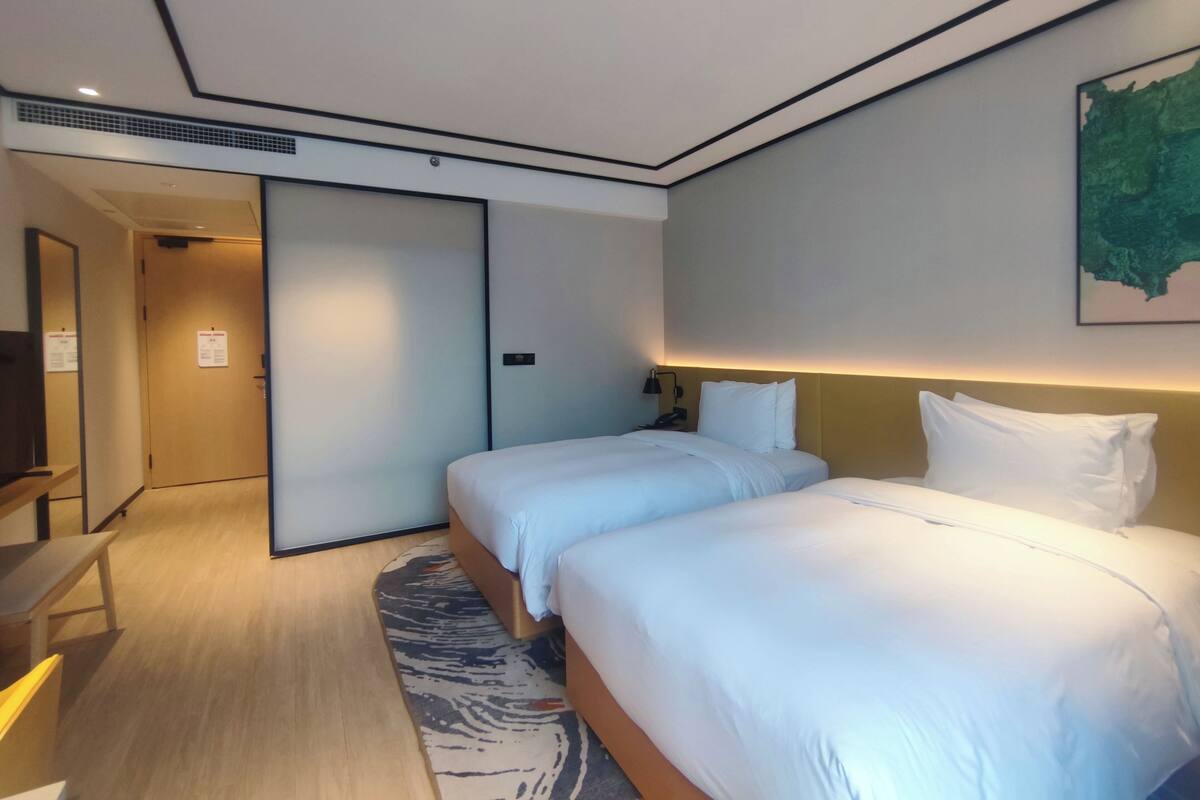 Habitació d'hotel amb dos llits, una taula de nit, una cadira, una làmpada d'escriptori i un quadre penjat a la paret.