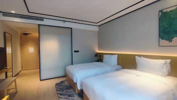 Habitación de hotel con dos camas, un escritorio, una silla, una lámpara de escritorio y un cuadro en la pared.