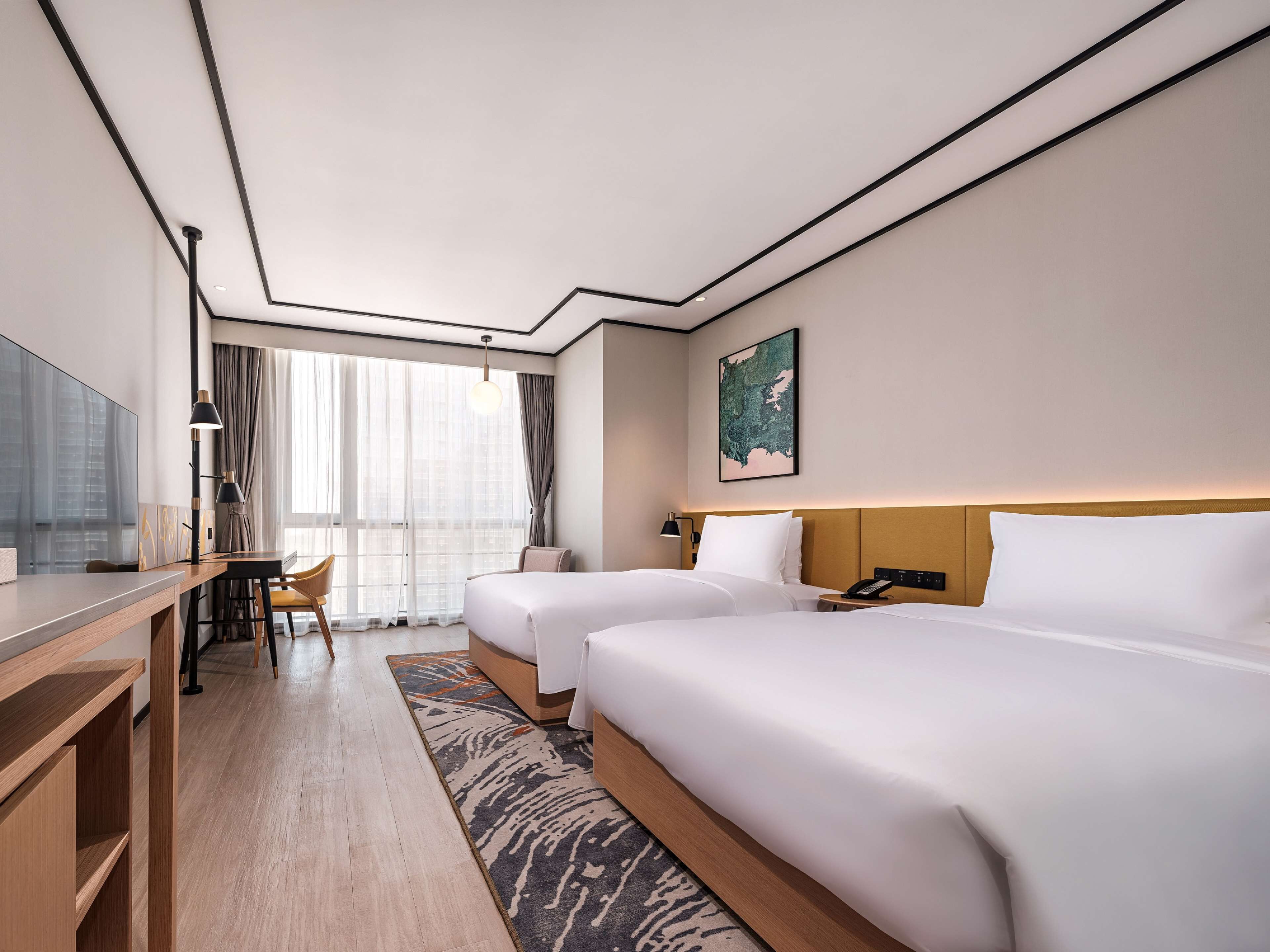 A hotel room with two beds, a desk, a chair, a TV, and a large window with curtains.