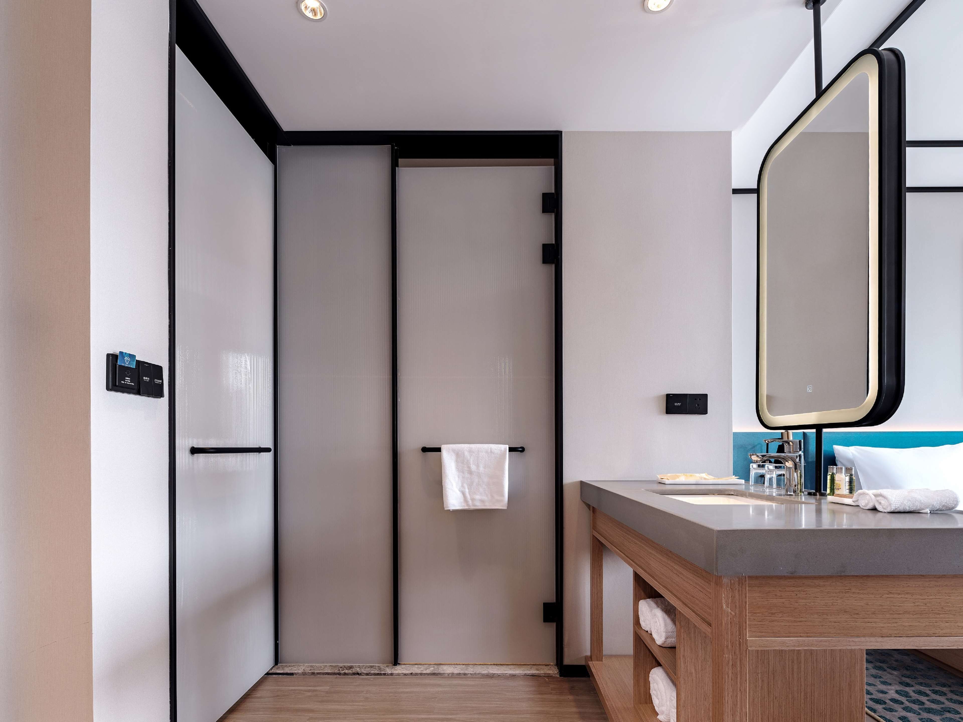 Une salle de bain moderne avec un meuble-lavabo en bois, un grand miroir et une serviette suspendue à un porte-serviettes.