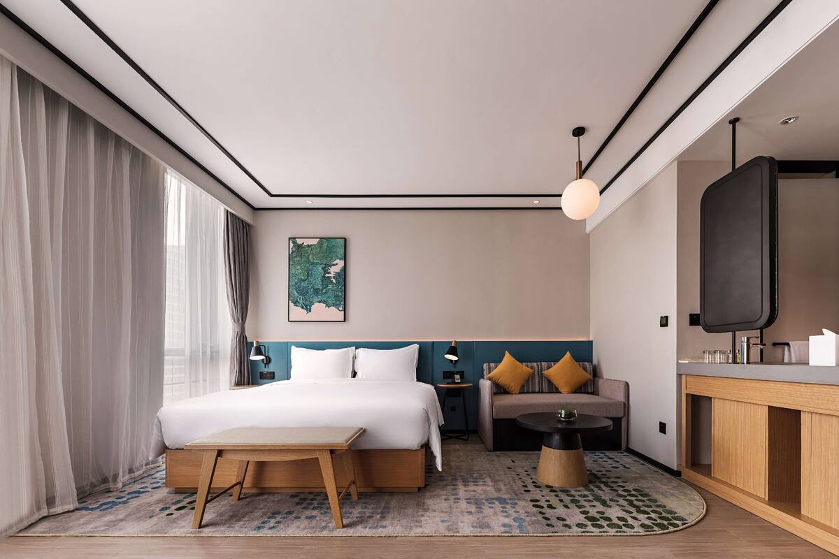 Habitació d'hotel moderna amb un llit gran, un sofà, una taula petita i una televisió.