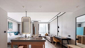 A modern hotel room with a wooden vanity, a large mirror, a sofa, a dining table, and a bed with a headboard. - Hilton Garden Inn Hefei Binhu New District (Hefei)