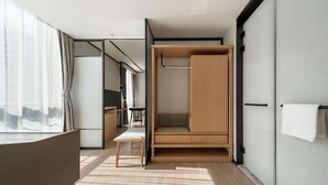 A modern hotel room with a minimalist design, featuring a wooden wardrobe, a small seating area, and a large window with sheer curtains. - Hilton Garden Inn Hefei Binhu New District (Hefei)