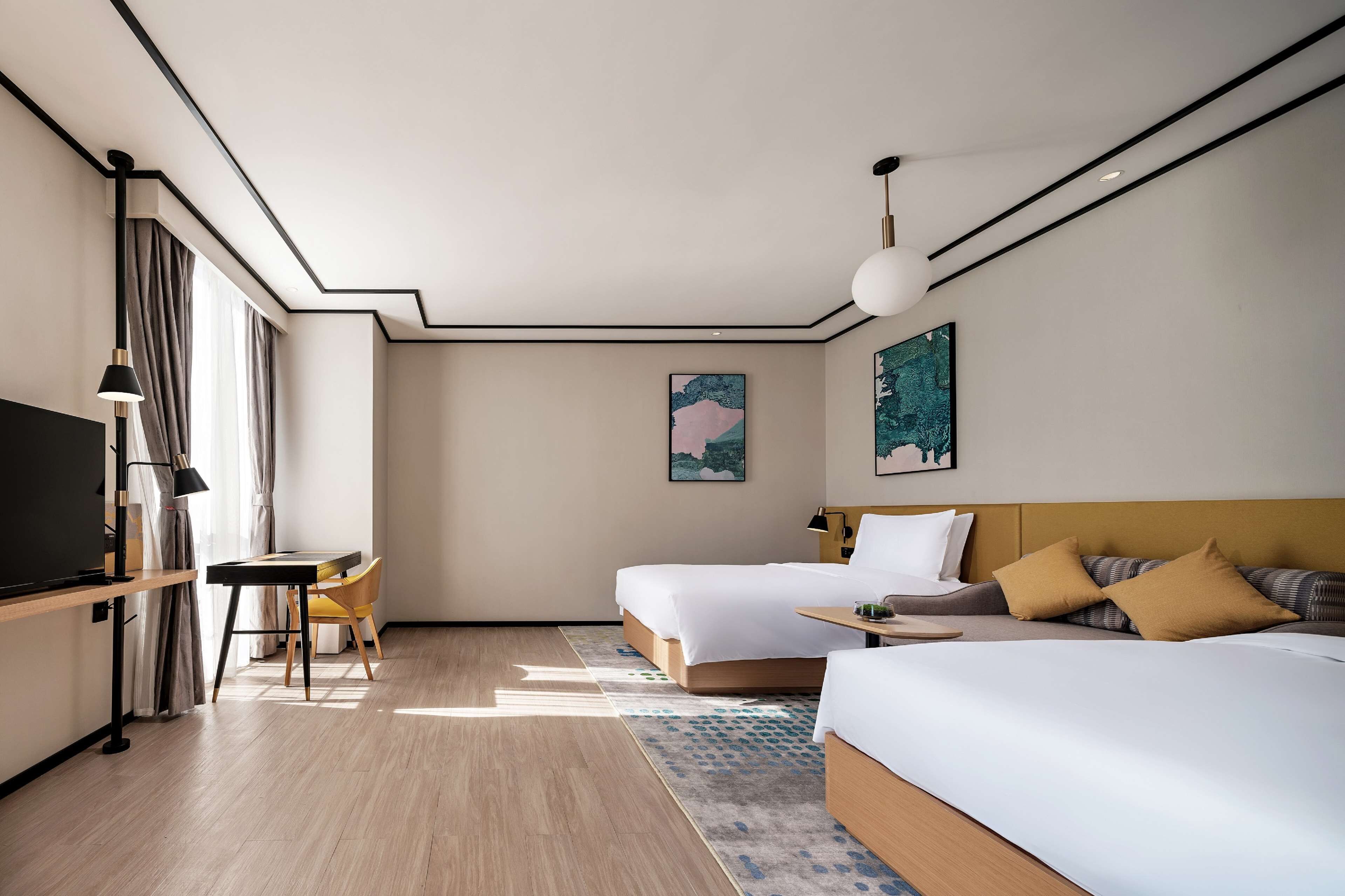 A modern hotel room with two beds, a desk, and a TV.