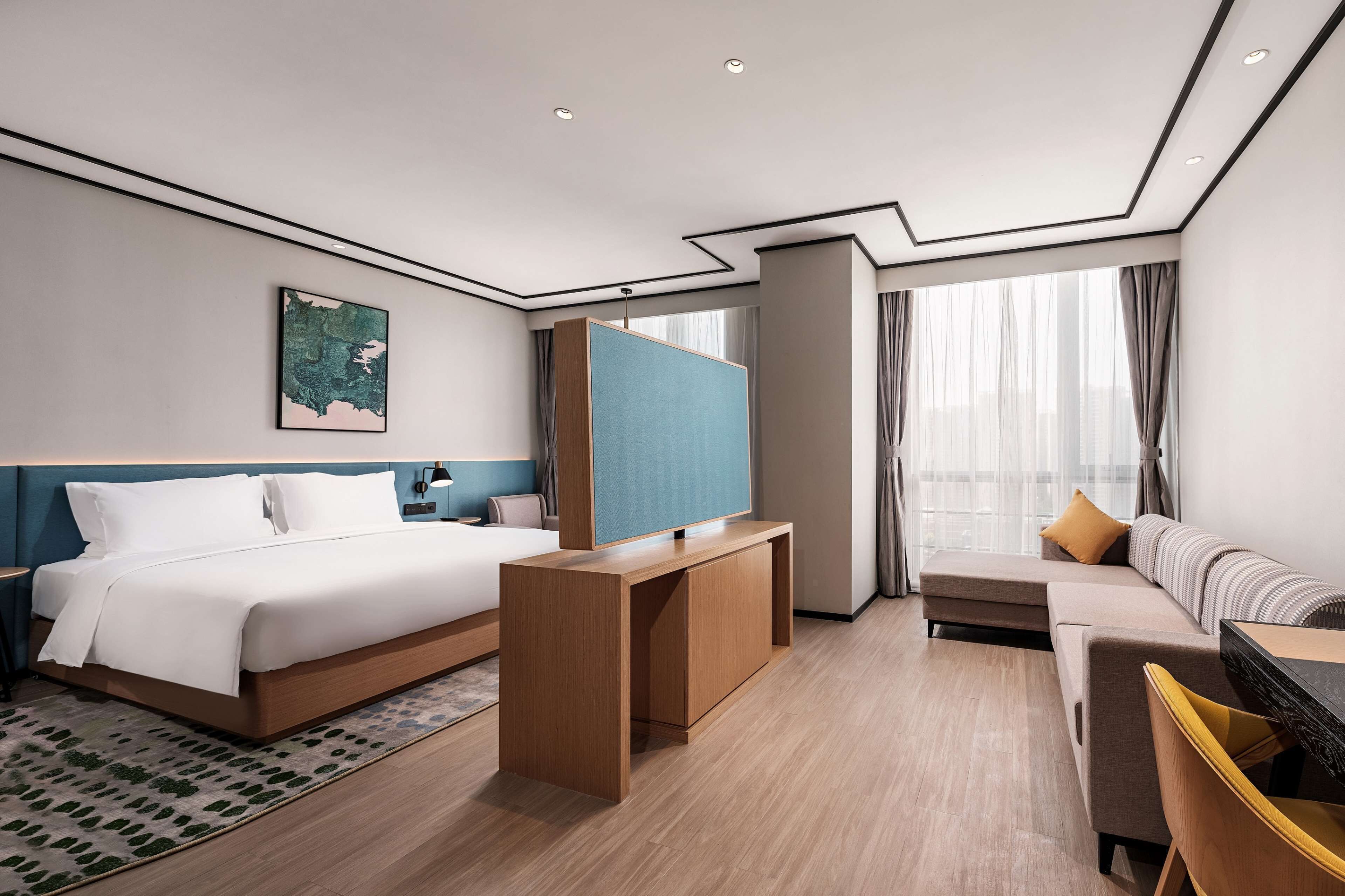 A modern hotel room with a large bed, a sofa, a TV, and a desk.