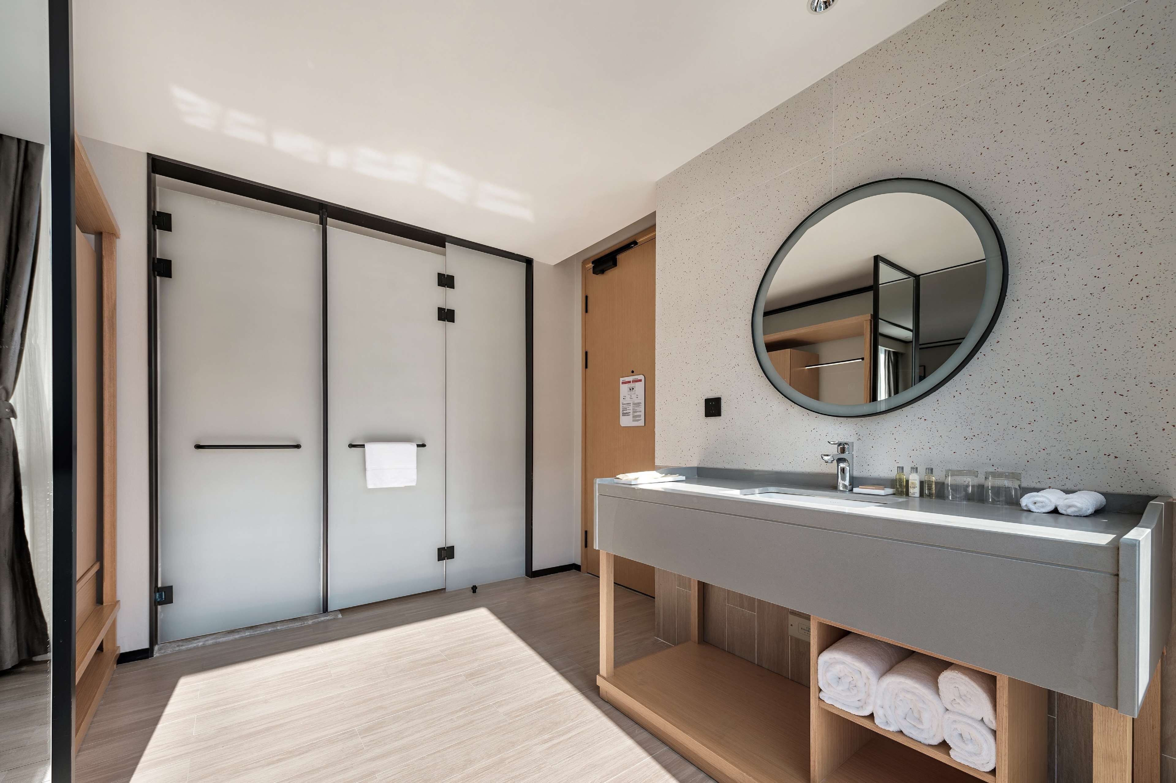 A modern bathroom with a large mirror, a sink with toiletries, and neatly rolled towels.