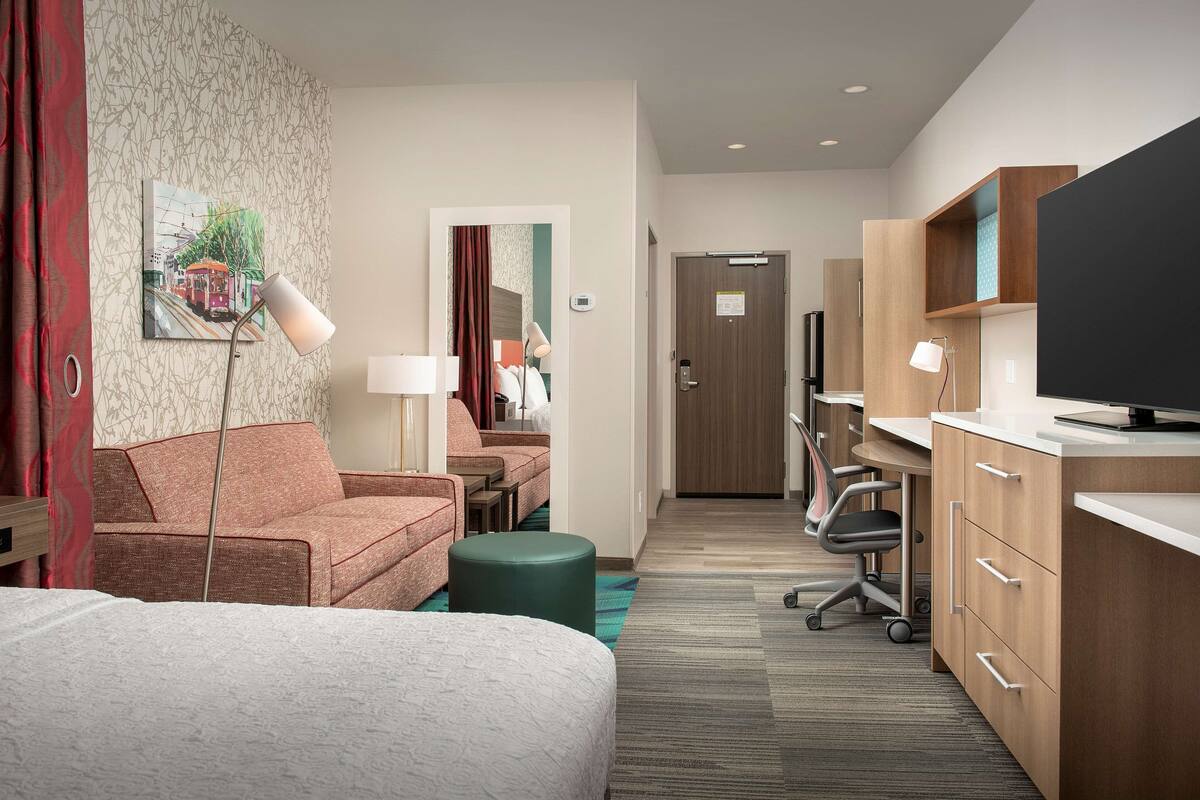 A hotel room with a bed, a desk, a chair, and a TV.