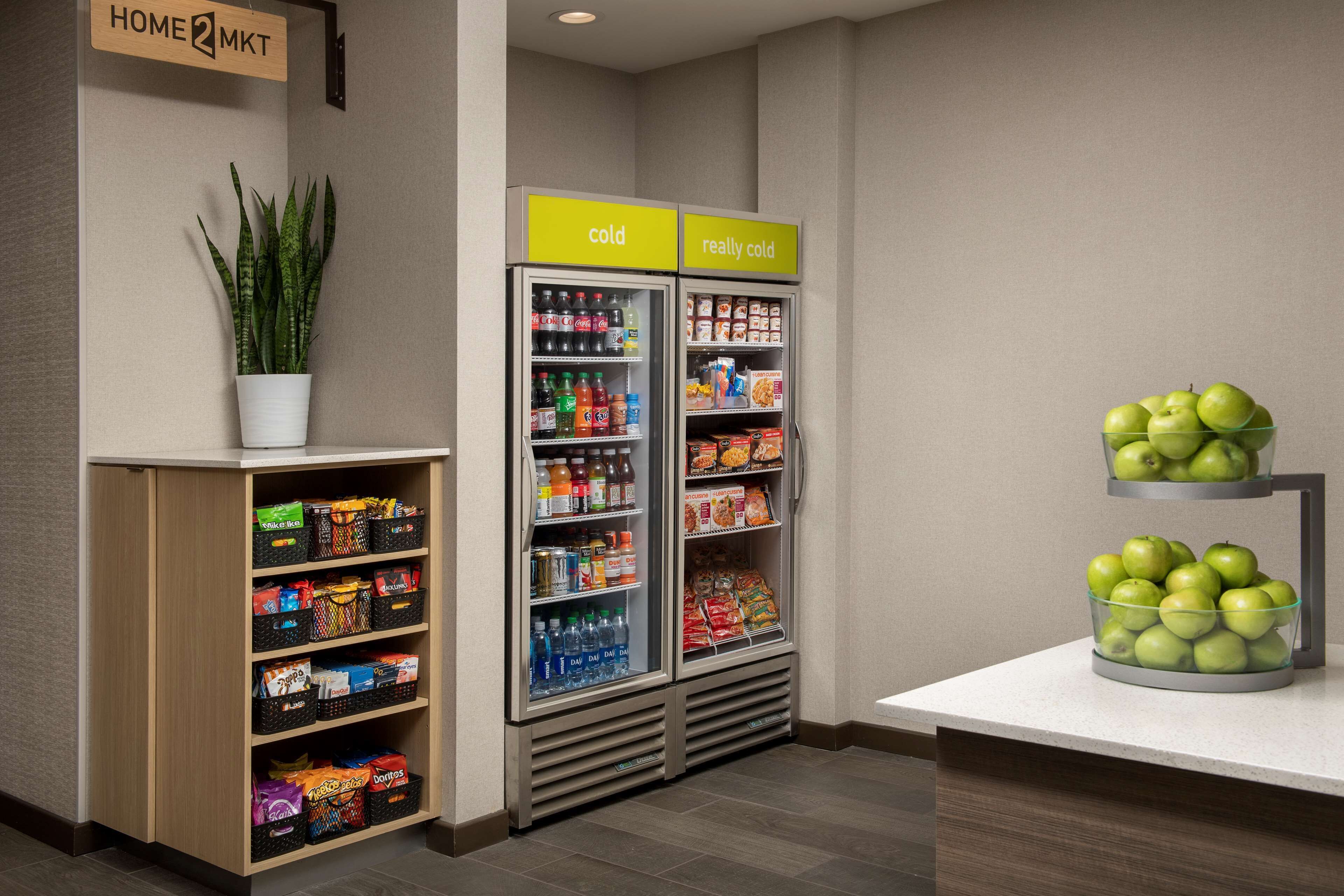 A kitchenette area with a refrigerator, a small shelf with snacks, and a bowl of apples.