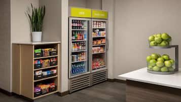 A kitchenette area with a refrigerator, a small shelf with snacks, and a bowl of apples.