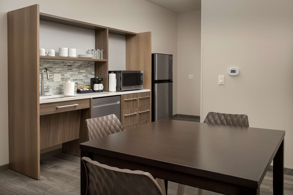 A modern kitchen with wooden cabinets, a stainless steel refrigerator, a microwave, and a dining area with a table and chairs.