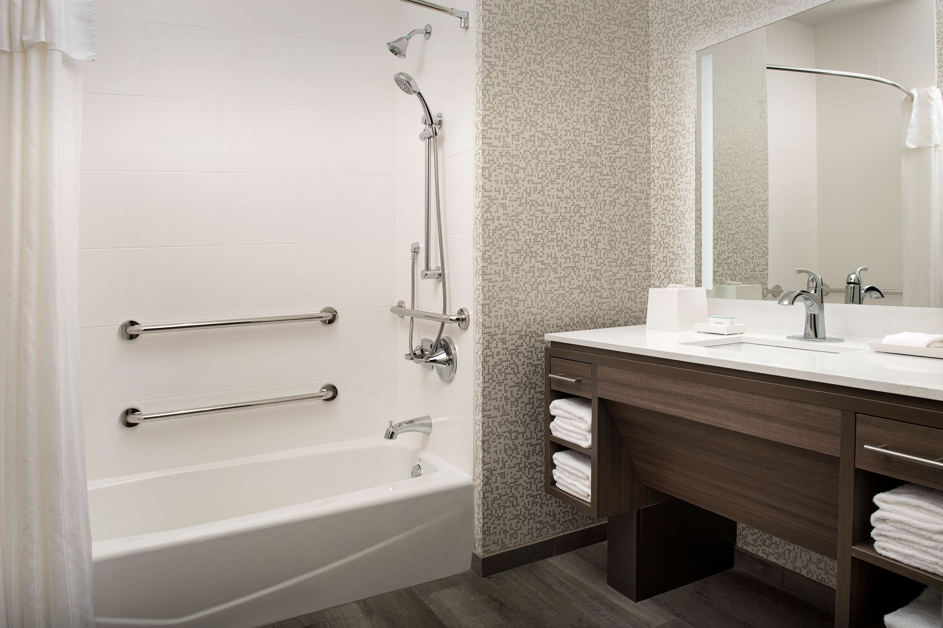 Un baño moderno con una bañera blanca, ducha con cabezal de mano, tocador con espejo y un perchero para toallas.