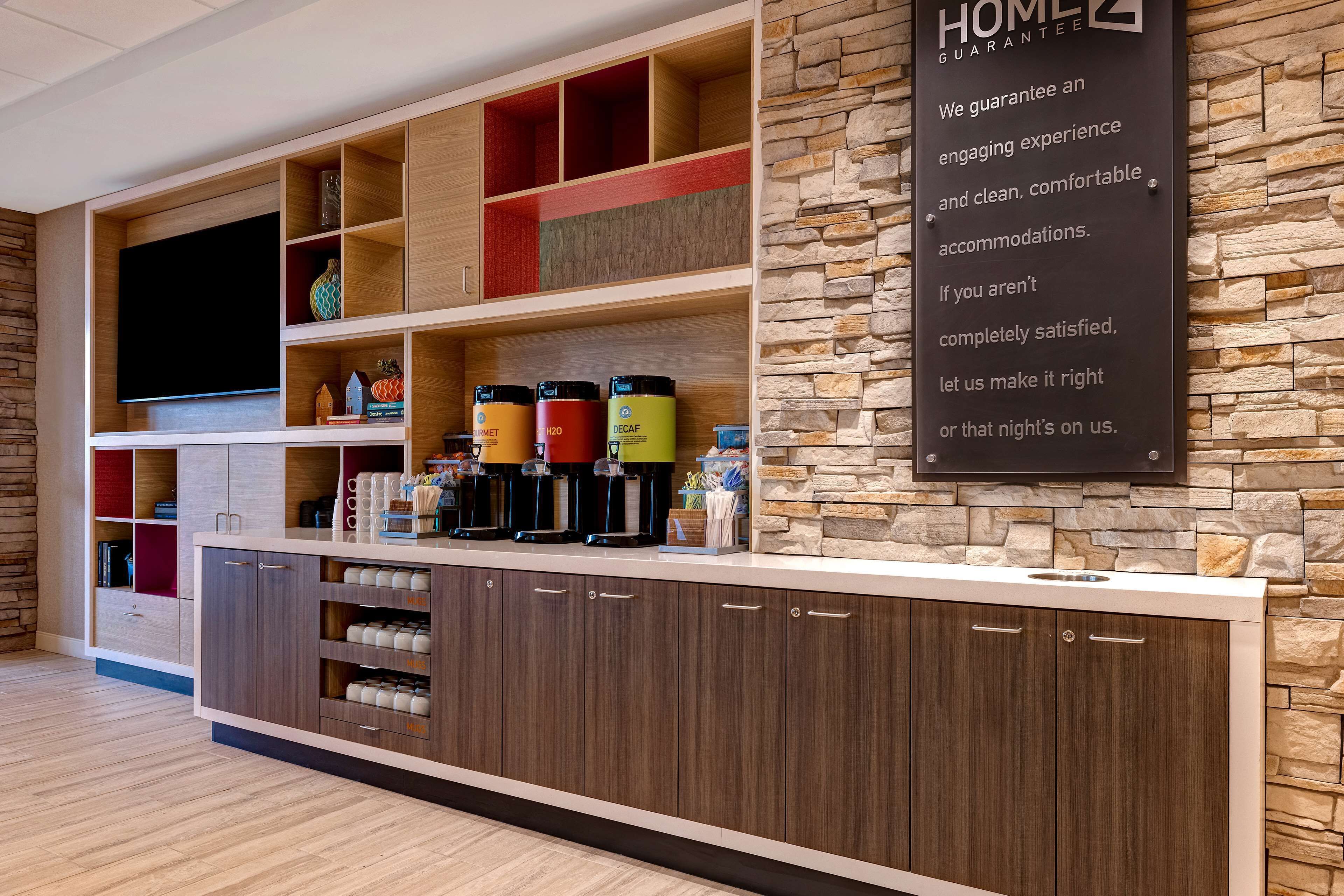 A modern hotel reception area with a stone wall, wooden shelving, and a flat-screen TV.