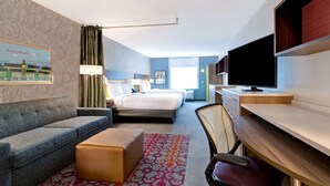 A hotel room with a sofa, a bed, a desk, a chair, and a television. - Home2 Suites by Hilton Lincolnshire Chicago (Lincolnshire)