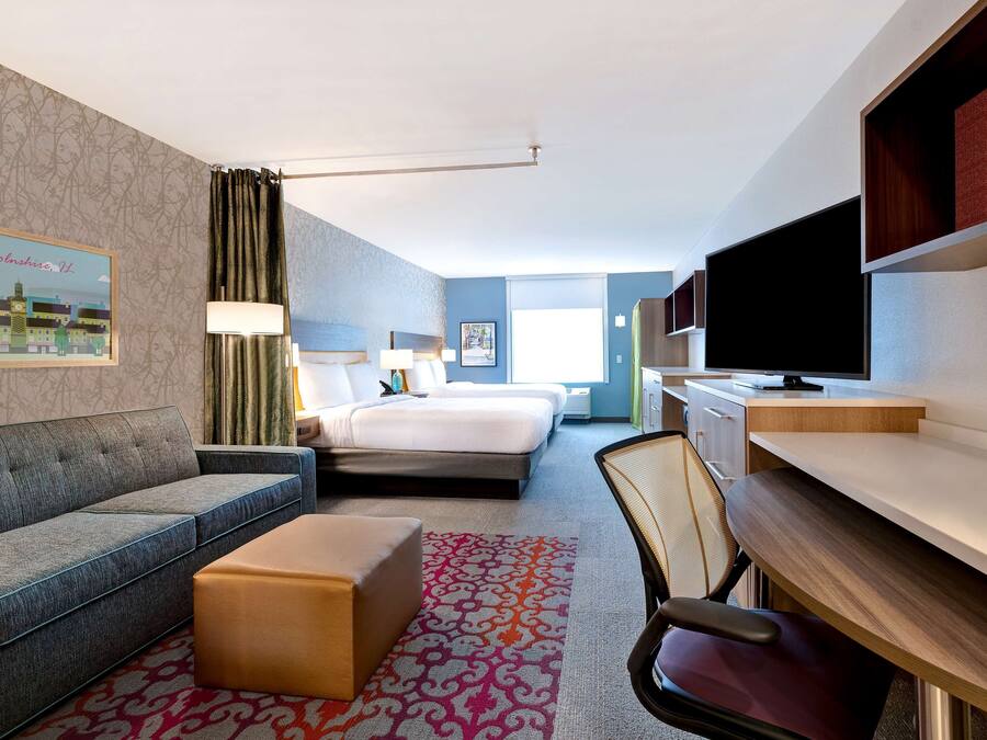 A hotel room with a sofa, a bed, a desk, a chair, and a television.