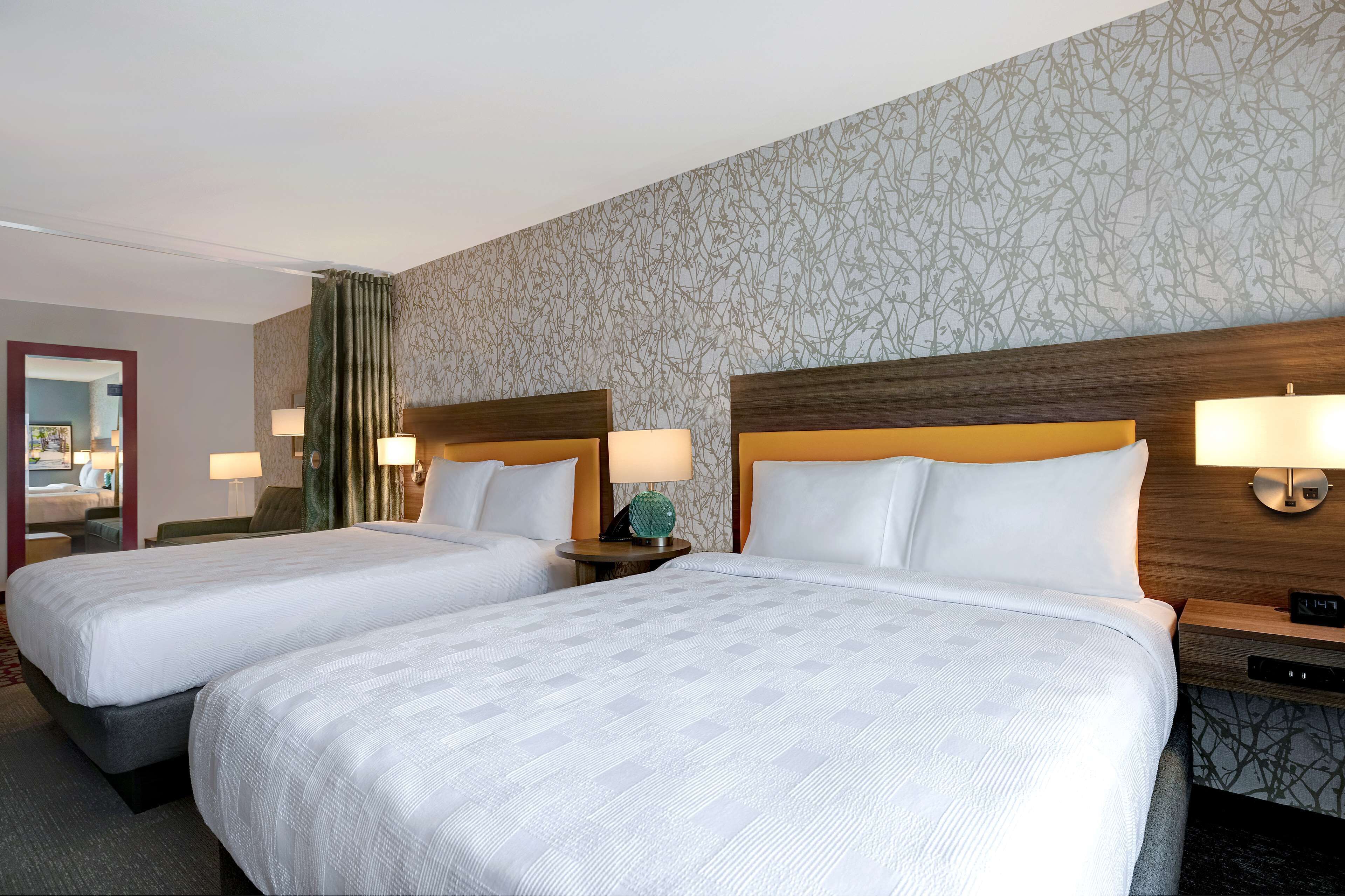 A hotel room with two beds, a wooden headboard, bedside lamps, and a patterned wallpaper.