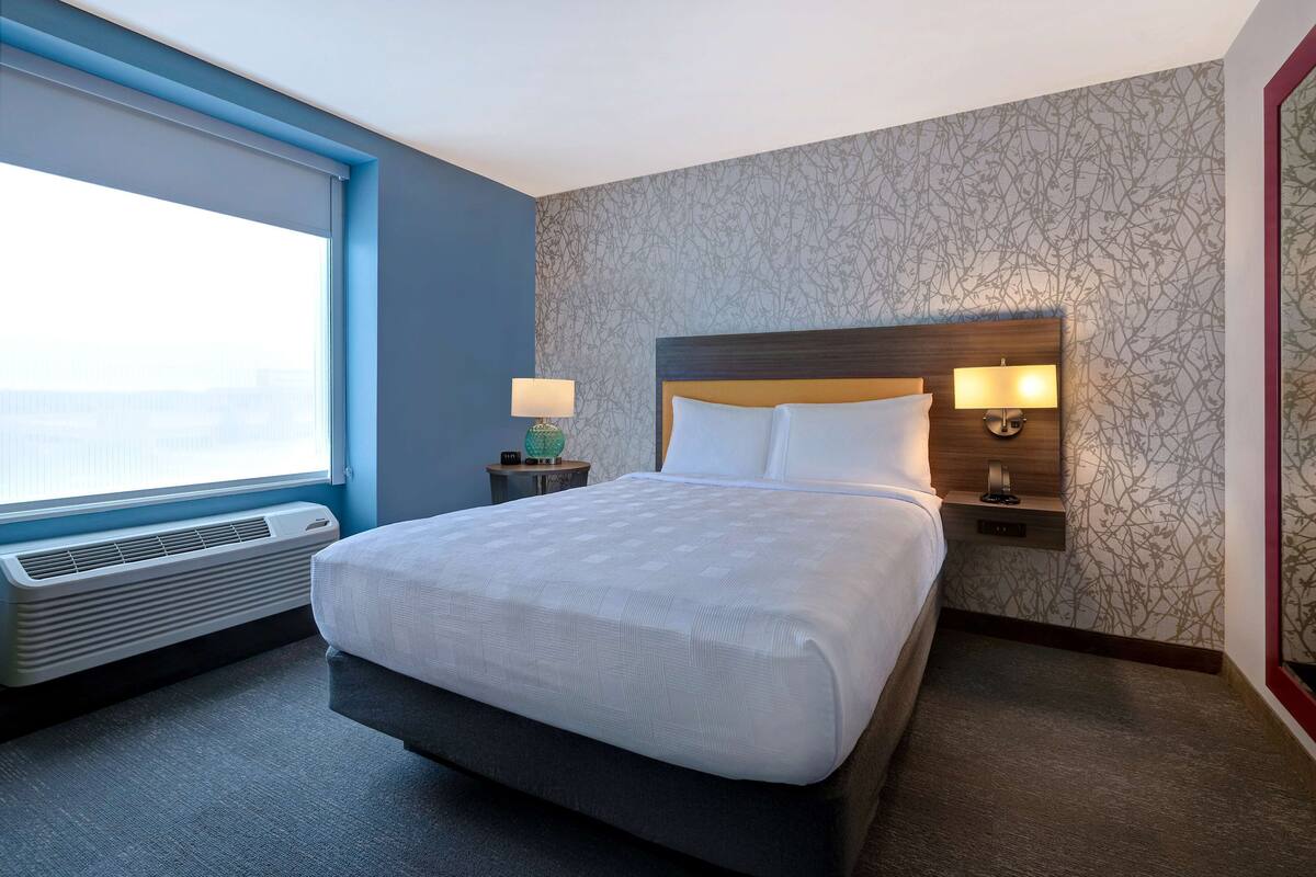 Camera d'albergo con un letto grande, una finestra con tende, un termosifone a parete e due lampade da comodino.